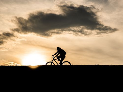 Zdję►cie przedstawia rowerzystkę na tle zachodzącego słońca. Jest to rowerzysta na ścieżce rowerowej na wałach wokół Jeziora Żywieckiego w Zarzeczu.
