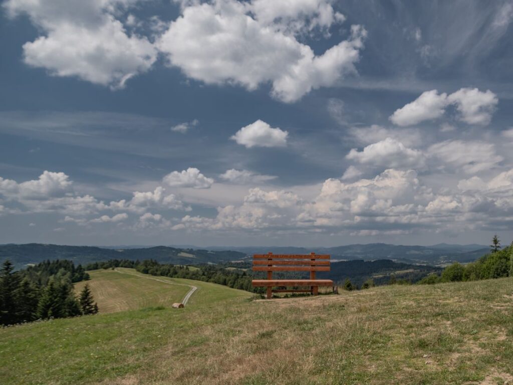 Zdjęcie przedstawia gigantyczną ławkę w Beskidach na tle malowniczych i pieknych widoków na góry.